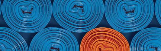 Mehrere aufgerollte blaue Matten von oben, eine orange Matte sticht farblich hervor, gleichmäßig angeordnet im Muster