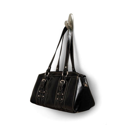 Numa bolsa de couro preta com alças duplas e fivelas decorativas pendurada num gancho de metal Command™ "clássico" da 3M Deutschland GmbH. A bolsa tem costuras brancas e uma superfície ligeiramente brilhante.