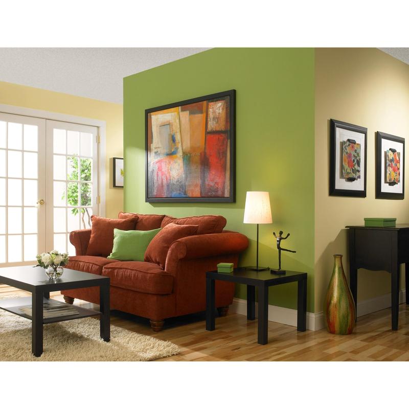 Uma sala de estar com paredes amarelas e verdes pintadas com fita de mascaramento ScotchBlue™ "Multi-Surface" da 3M Deutschland GmbH, um sofá vermelho com almofadas verdes, uma mesa de centro preta, uma mesa lateral com lâmpada, arte abstrata, piso de madeira e portas de vidro.