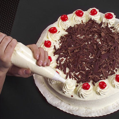 Com o Starpak 10 saco de confeitar de 1,8 l com 3 bicos, um bolo redondo é decorado com chantilly aplicado, raspas de chocolate no meio e cerejas no topo, colocado sobre um doily branco em um fundo escuro.