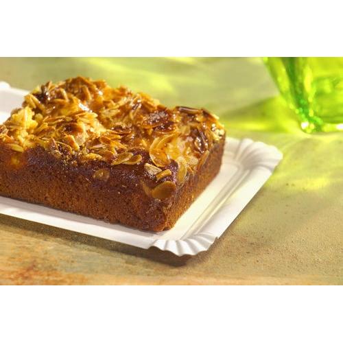 Um bolo de amêndoa quadrado repousa sobre um PAPSTAR GmbH prato retangular 24x33 cm, papelão "pure", branco (125 unidades), com um objeto de vidro verde que se desfoca ao fundo.