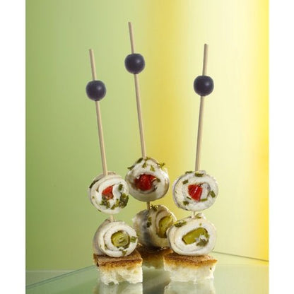 Três PAPSTAR 250 palitos de finger food da PAPSTAR GmbH seguram pãezinhos de queijo, ervas e vegetais em cubos de pão, cada um decorado com uma azeitona preta. O fundo suavemente iluminado é em tons de verde e amarelo.