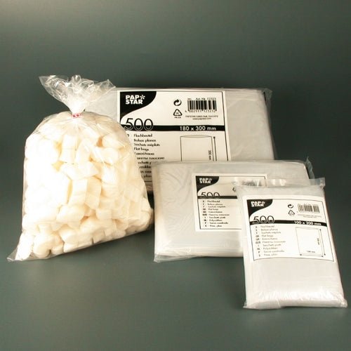 Um conjunto de produtos da PAPSTAR GmbH, composto por um saco de açúcar em cubos branco e três embalagens de PAPSTAR 500 sacos planos LDPE transparentes em vários tamanhos, apresentados sobre um fundo cinza simples como soluções de embalagem transparentes.