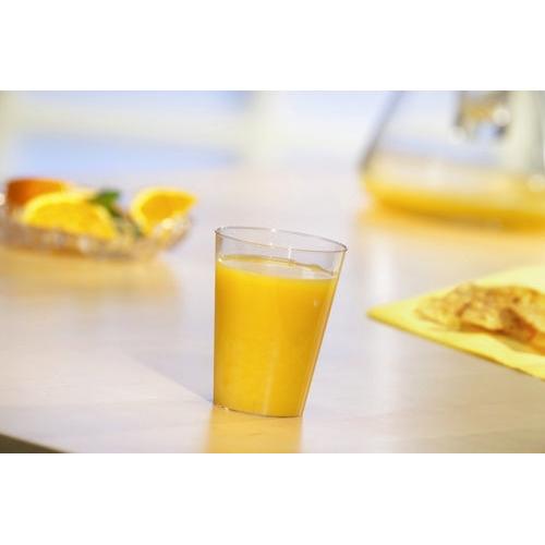 Um copo Starpak 40, PS 0,1 l Ø 5,5 cm · 7,5 cm, copo descartável transparente está cheio de suco de laranja sobre uma mesa clara. Ao fundo, fatias de laranja e um jarro – ideal para festas e eventos.