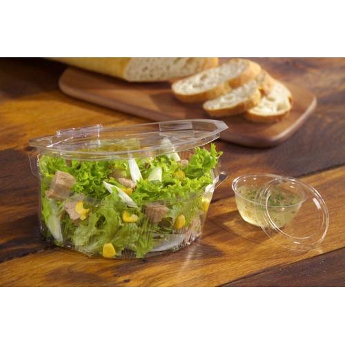 Uma tampa Starpak 100 clara e redonda (PS, Ø 6,7 cm, 1 cm de altura) fecha um recipiente de plástico com salada verde, milho e carne, ao fundo está uma baguete cortada sobre uma tábua de madeira.