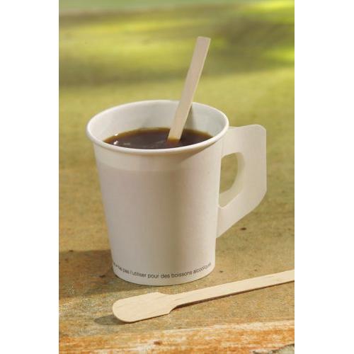 Sobre uma superfície, há um copo de papel branco com café preto, dentro dele uma PAPSTAR colher de mexer "pure" da PAPSTAR GmbH, com outra colher de mexer naturalmente clara ao lado, diante de um fundo suavemente desfocado.