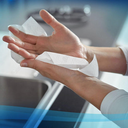Uma pessoa seca as mãos sobre uma pia de cozinha com toalhas de papel Scott® Essential™ 6638 de 1-camada da Kimberly-Clark GmbH; a imagem é cercada por uma borda azul suave.