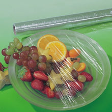 Uma tigela de plástico transparente com uvas, morangos, laranjas e carambolas está coberta com película aderente perfurada da Starpak. Atrás da tigela, há um rolo desta película aderente perfurada sobre uma superfície verde.