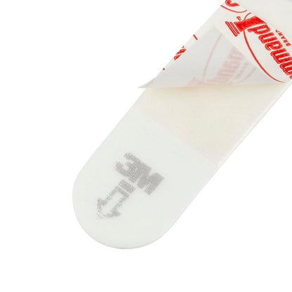 Uma imagem de close-up de uma Pequena Tira Command™ S, 17022N da 3M Deutschland GmbH mostra sua forma retangular, com uma extremidade do papel protetor removida, revelando o adesivo. "MC" e uma seta estão impressos para permitir um uso fácil e sem danos na parede.
