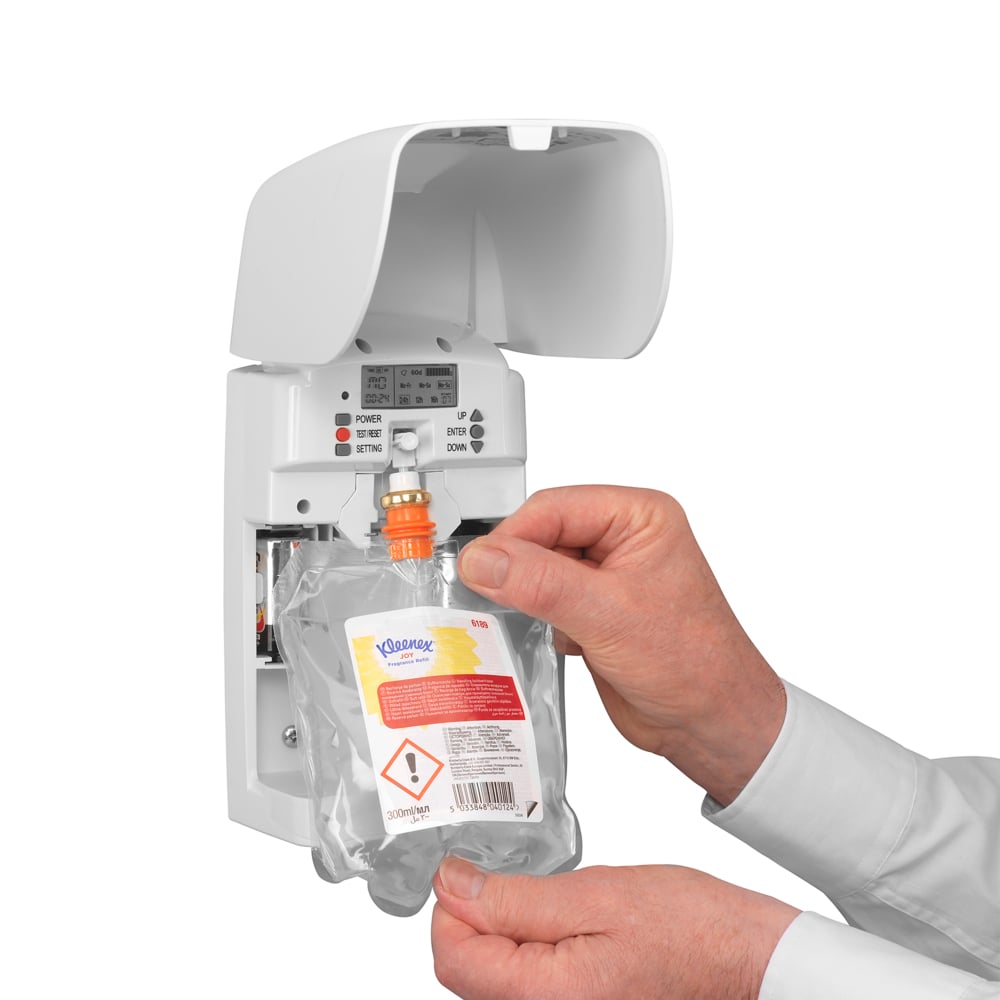 Uma pessoa insere uma recarga Kleenex® Duft Joy (300 ml, Transparente) da Kimberly-Clark GmbH em um dispensador de parede branco, garantindo frescor duradouro com botões e indicadores visíveis.