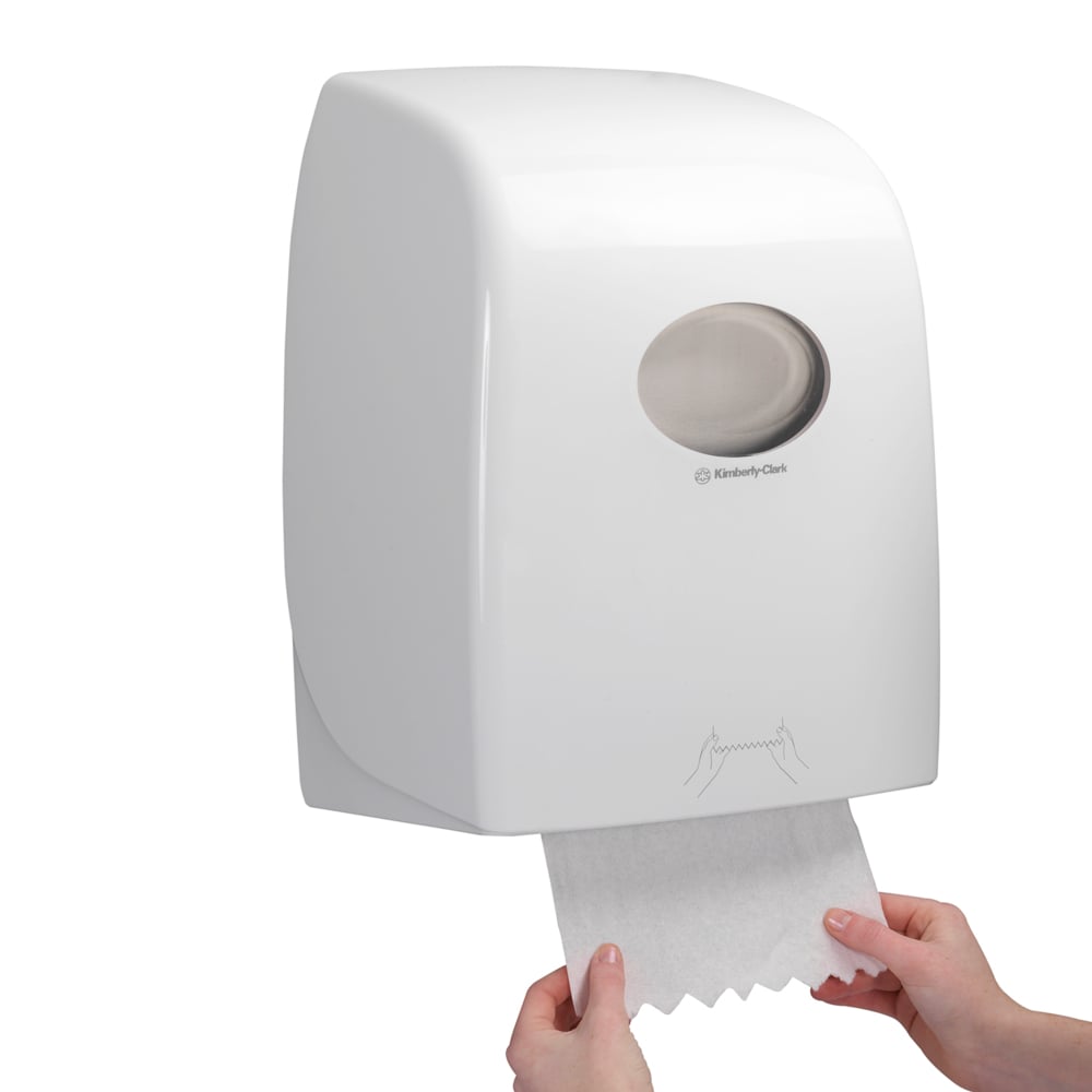 Alguém puxa uma folha de Toalhas Scott® ESSENTIAL™ - Rolo de um dispensador branco montado na parede da Kimberly-Clark GmbH, cuja janela transparente oferece uma visão dos rolos de toalha no interior.
