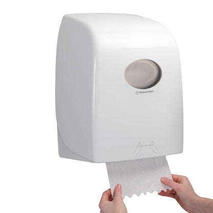 Alguém puxa uma folha de Toalhas Scott® ESSENTIAL™ - Rolo de um dispensador branco montado na parede da Kimberly-Clark GmbH, cuja janela transparente oferece uma visão dos rolos de toalha no interior.