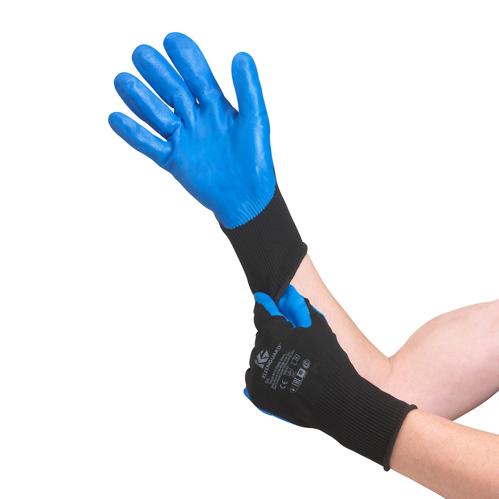Eine Person, die blaue KleenGuard® G40 Nitril-Handschuhe der Kimberly-Clark GmbH trägt, streift sich einen Chemikalienschutzhandschuh über die rechte Hand vor einem weißen Hintergrund.