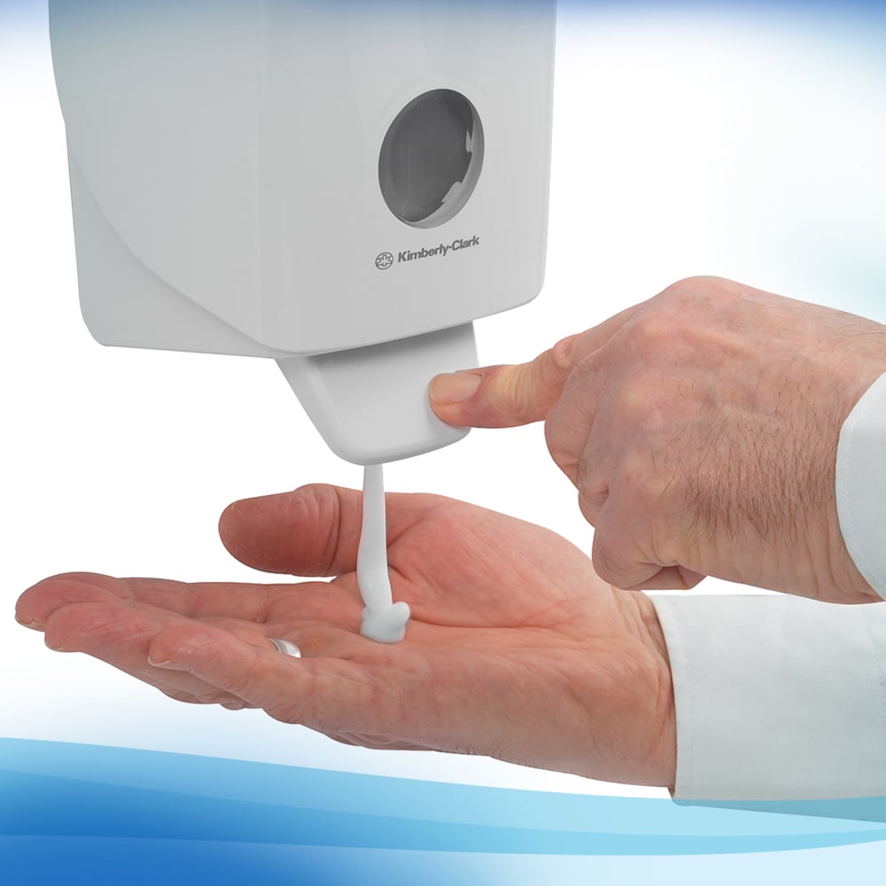 Uma pessoa com uma camisa branca de mangas compridas pressiona um dispensador de espuma de limpeza para mãos Kimberly-Clark Scott® Control™ de 1L - ideal para uso frequente.