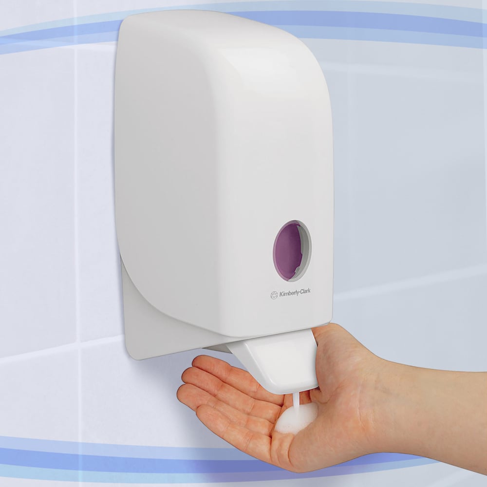 Uma pessoa dispensa sabão em espuma de um dispensador branco Aquarius™ para loções de lavagem - cartucho / 1 Ltr da Kimberly-Clark GmbH em sua mão em um banheiro revestido de azulejos.
