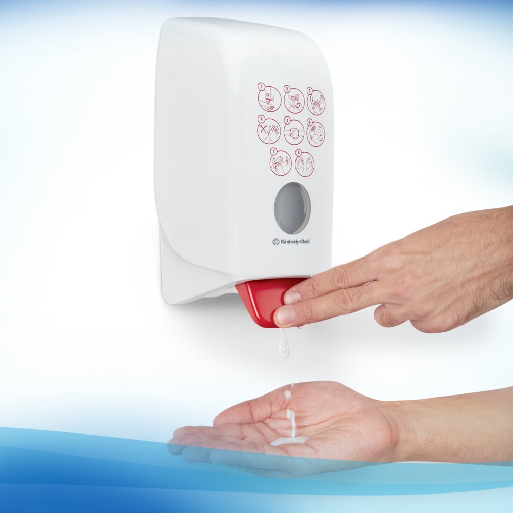 O usuário pressiona a alavanca da Espuma Desinfetante para as Mãos à Base de Álcool Scott® CONTROL (cartucho de 1L) da Kimberly-Clark GmbH e aplica a espuma na mão. Na frente da unidade de parede transparente, há símbolos de higiene das mãos.