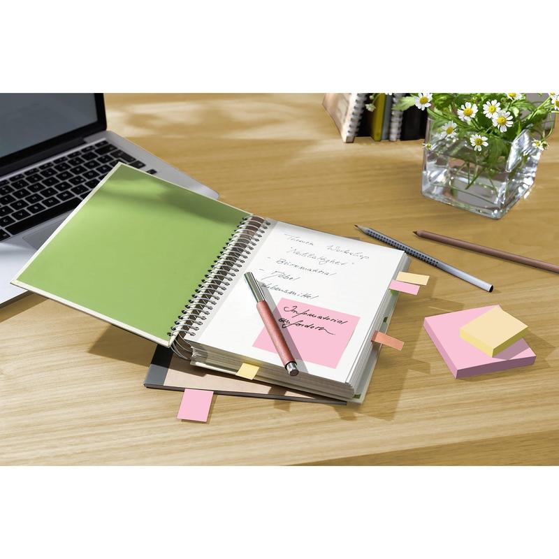 Um caderno com anotações manuscritas e notas recicladas 3M Post-it® (38 mm x 51 mm, 100% PEFC) está aberto sobre uma mesa de madeira ao lado de um laptop, canetas e um vaso com margaridas brancas.