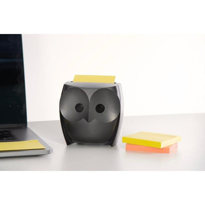 Um dispensador de notas Post-it® Z-Notes em forma de coruja, preto, da 3M segura notas Super Sticky Z-Notes amarelas. Ao lado estão um laptop fechado e um pacote com notas amarelas e rosas (2 blocos de 45 folhas) sobre uma mesa branca.