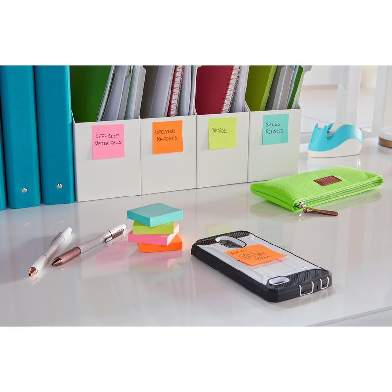Na mesa de trabalho arrumada estão pastas rotuladas, um estojo verde, duas canetas e um smartphone com um Post-it® Super Sticky Note (76x127 mm, 3M Deutschland GmbH), onde está escrito "AM Call Client Chet". A superfície bem iluminada é branca.