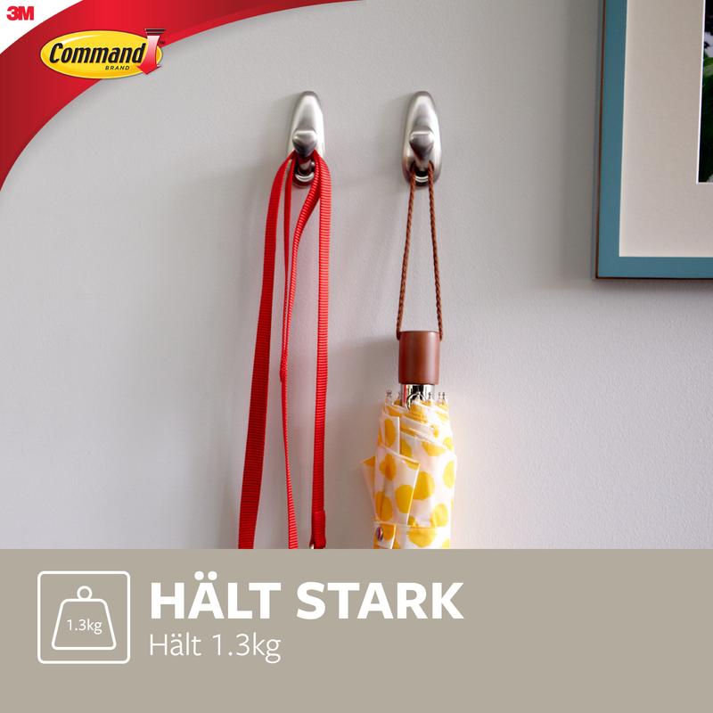 Dois ganchos de metal Command™ "clássico" da 3M Deutschland GmbH estão montados numa parede branca e seguram uma trela vermelha e um guarda-chuva amarelo com padrões. O texto diz: "SEGURA FORTEMENTE Suporta 1.3kg" e mostra o logotipo Command.
