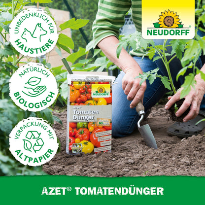 Uma pessoa usa uma colher de jardinagem perto de plantas de tomate e tem uma caixa de Azet TomatenDünger da Neudorff Shop. Ícones ecológicos e amigáveis para animais de estimação destacam este fertilizante orgânico para "uma colheita abundante".