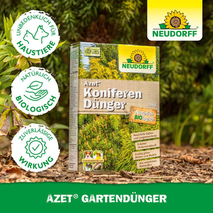 Uma caixa de Neudorff Shop Azet KoniferenDünger está ao ar livre no chão entre coníferas verdes. A embalagem alemã destaca suas propriedades naturais, biológicas e amigáveis para animais de estimação, tornando-o ideal para plantas perenes e barreiras visuais.