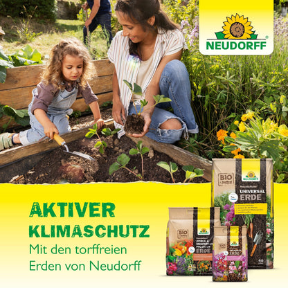 Uma mulher e uma menina jardineiam juntas ao ar livre, plantando mudas em um canteiro elevado com uma espátula. Em primeiro plano, há sacos de NeudoHum Aussaat- & KräuterErde da Neudorff Shop - ideal para flores e vegetais.
