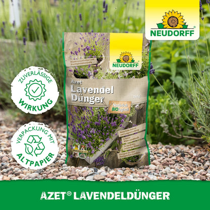 Um saco de Neudorff Shop Azet LavendelDünger está em um caminho de jardim de cascalho ao lado de lavanda com flores azul-violeta. Na embalagem está escrito "ambientalmente amigável" em alemão.