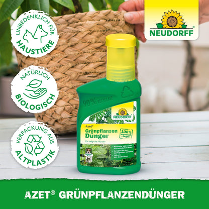 Uma garrafa verde da Neudorff Shop Azet GrünpflanzenDünger líquido está em uma mesa ao lado de uma planta em vaso. No rótulo estão os nutrientes para plantas verdes, segurança para animais de estimação, ingredientes naturais e embalagens recicladas. Ao fundo, vê-se uma mão.