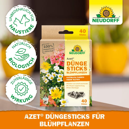Uma caixa de Azet Düngesticks para plantas com flores do Neudorff Shop (40 sticks) é mostrada em frente a flores floridas. A embalagem enfatiza a segurança para animais de estimação, os ingredientes naturais e a eficácia confiável.