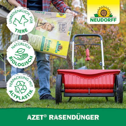 Uma pessoa enche um espalhador vermelho com Neudorff Shop Azet RasenDünger 2,5-5 kg, para promover áreas de relva densas. Três símbolos indicam que é amigo dos animais, biologicamente natural e feito de plástico reciclado. O logotipo Neudorff é visível.