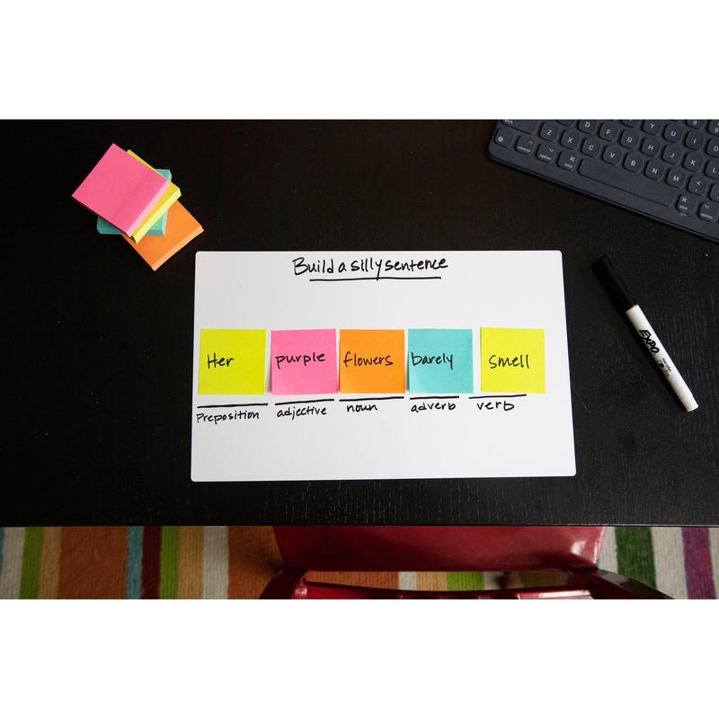 Um bloco de notas Post-it® da 3M Deutschland GmbH (76x76mm, 450 folhas, 100% PEFC) mostra uma tarefa de construção de frases em um quadro branco com etiquetas gramaticais; notas adesivas adicionais, um marcador, um teclado e um tapete listrado estão por perto.