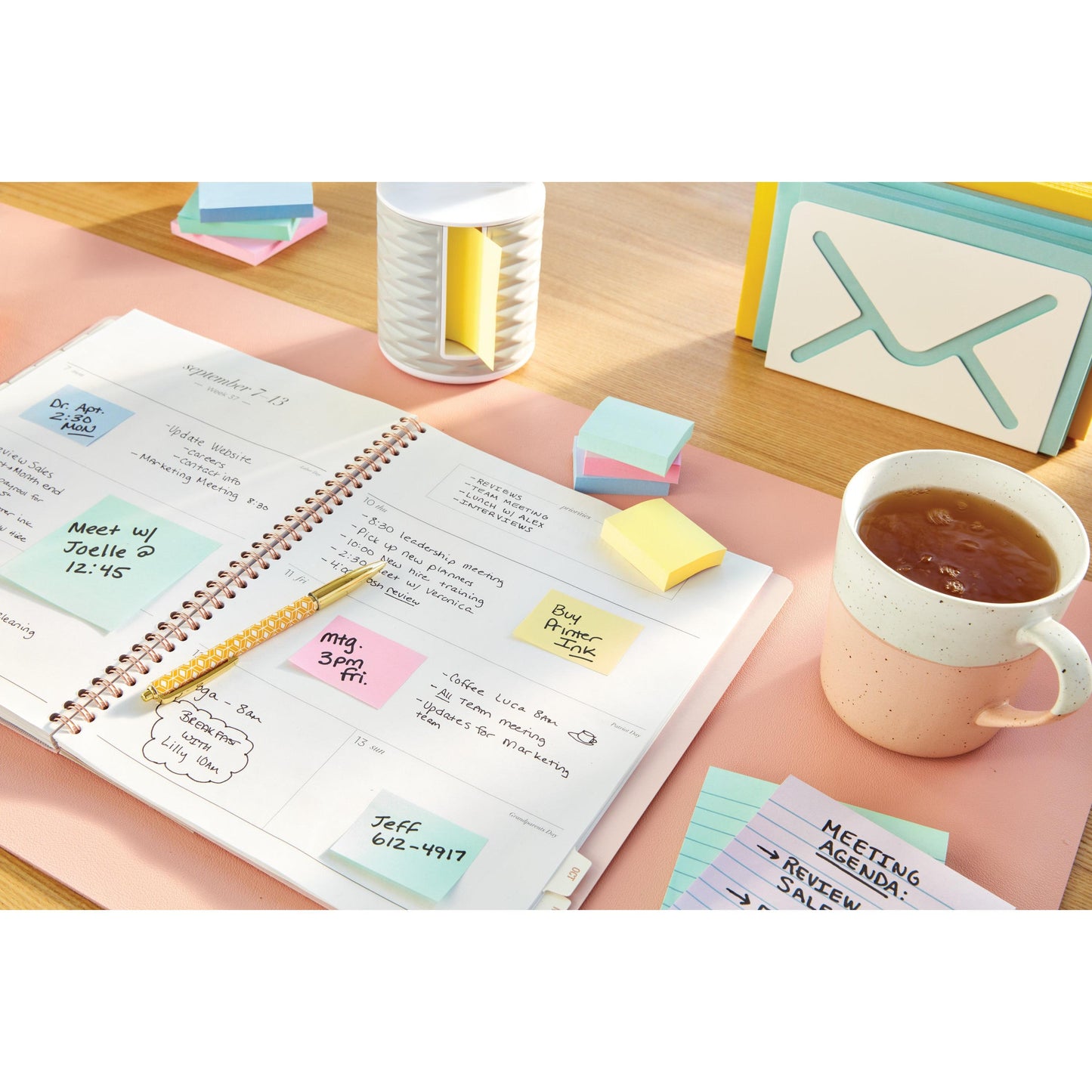 Um planejador com anotações manuscritas e Notas Post-it® da 3M (38x51 mm, Amarelo, 100 folhas/bloco, 16+4 Grátis) está sobre uma mesa ao lado de uma caneca, um lápis, pilhas de notas adesivas coloridas, um organizador e cartões de notas.