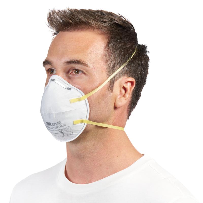 Um homem com cabelo castanho curto usa uma máscara de partículas 3M™ 8710E FFP1 (da 3M Deutschland GmbH) com faixas amarelas e sem válvula sobre o nariz e a boca, combinado com uma camisa branca simples sobre um fundo branco.