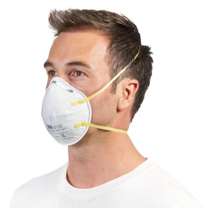 Um homem com cabelo castanho curto usa uma máscara de partículas 3M™ 8710E FFP1 (da 3M Deutschland GmbH) com faixas amarelas e sem válvula sobre o nariz e a boca, combinado com uma camisa branca simples sobre um fundo branco.