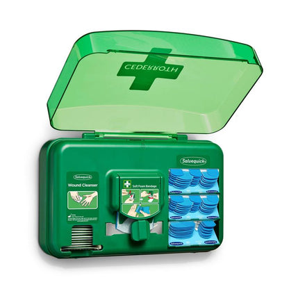 Um dispensador de cuidados de feridas azul da Orkla Wound Care AB está aberto e revela pacotes de limpeza de feridas, pensos e um rolo de ataduras de espuma macia, organizados em compartimentos individuais.