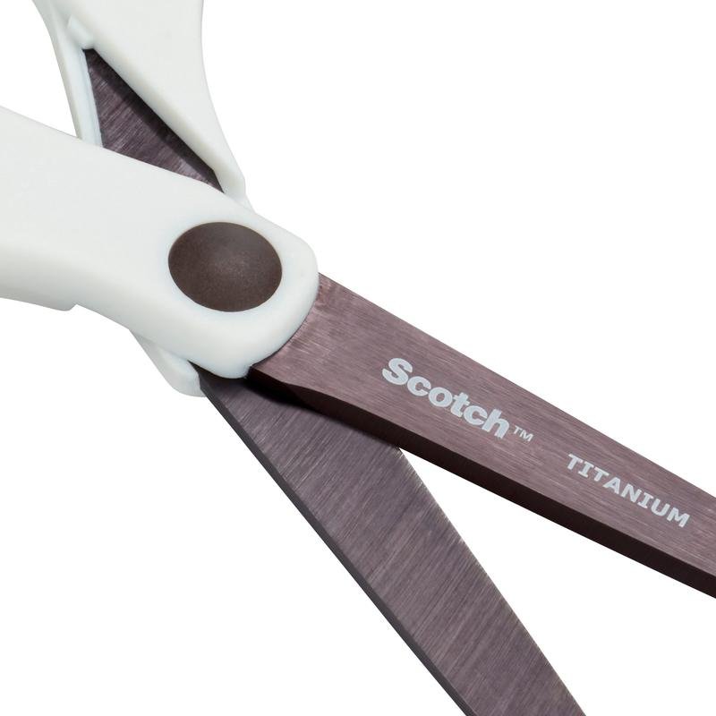 Close de um par de tesouras Scotch™ Titanium (20 cm) da 3M Deutschland GmbH com cabos brancos e lâminas de titânio. Em uma lâmina estão impressos "Scotch" e "Titanium" em branco.