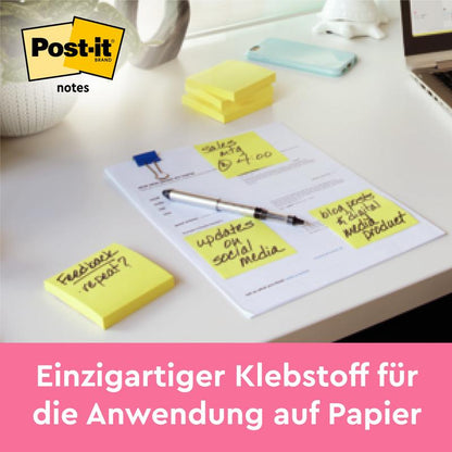 Uma pilha de Post-it® Notes, Amarelo, 38 mm x 51 mm (100 folhas/bloco, 12 blocos/embalagem) da 3M Deutschland GmbH está sobre uma mesa; ao lado, quatro papéis com texto manuscrito estão presos a uma folha. O logotipo Post-it e o slogan alemão são visíveis.
