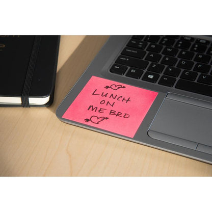 Um bloco de notas Post-it® (76x76mm, 450 folhas, 100% PEFC) da 3M Deutschland GmbH em rosa está sobre um teclado de laptop com "ALMOÇO POR MINHA CONTA" e rabiscos de corações. Um caderno preto fechado está ao lado em uma mesa de madeira clara.