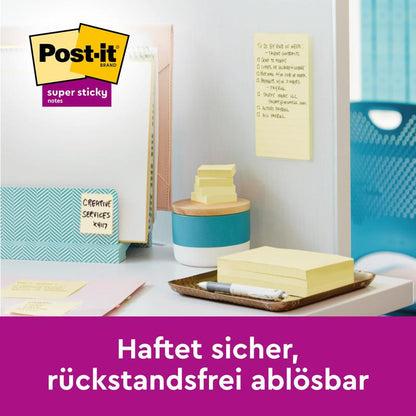 Uma área de trabalho com Post-it® Super Sticky Z-Notes, Amarelo, 76 mm x 76 mm da 3M Deutschland GmbH (90 folhas/bloco, 12 blocos/pacote) é mostrada na mesa e na parede. Lista de tarefas visível em notas adesivas amarelas. Texto: "Adere com segurança, removível sem deixar resíduos.