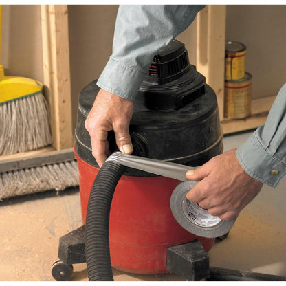 Uma pessoa envolve a fita adesiva universal Scotch® 2904 (10 m x 48 mm) da 3M Deutschland GmbH em torno da conexão da mangueira de um aspirador de pó úmido/seco vermelho e preto, ao fundo vê-se uma vassoura e latas de tinta.