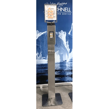 Um suporte de dispensador de desinfetante em aço inoxidável com uma bandeja de gotejamento da DR.SCHNELL GmbH & Co. KGaA Dr. Schnell para dispensadores e uma tela de instruções digital está posicionado diante de icebergs e do mar, criando uma atmosfera clara e moderna.