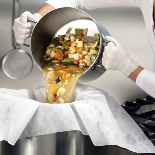 Vestida com luvas brancas, alguém despeja vegetais e caldo através de panos de passar e filtrar forrados com pergaminho (100x100 cm, 10 unidades) da Starpak em um grande recipiente de metal, demonstrando assim a aplicação prática na cozinha.