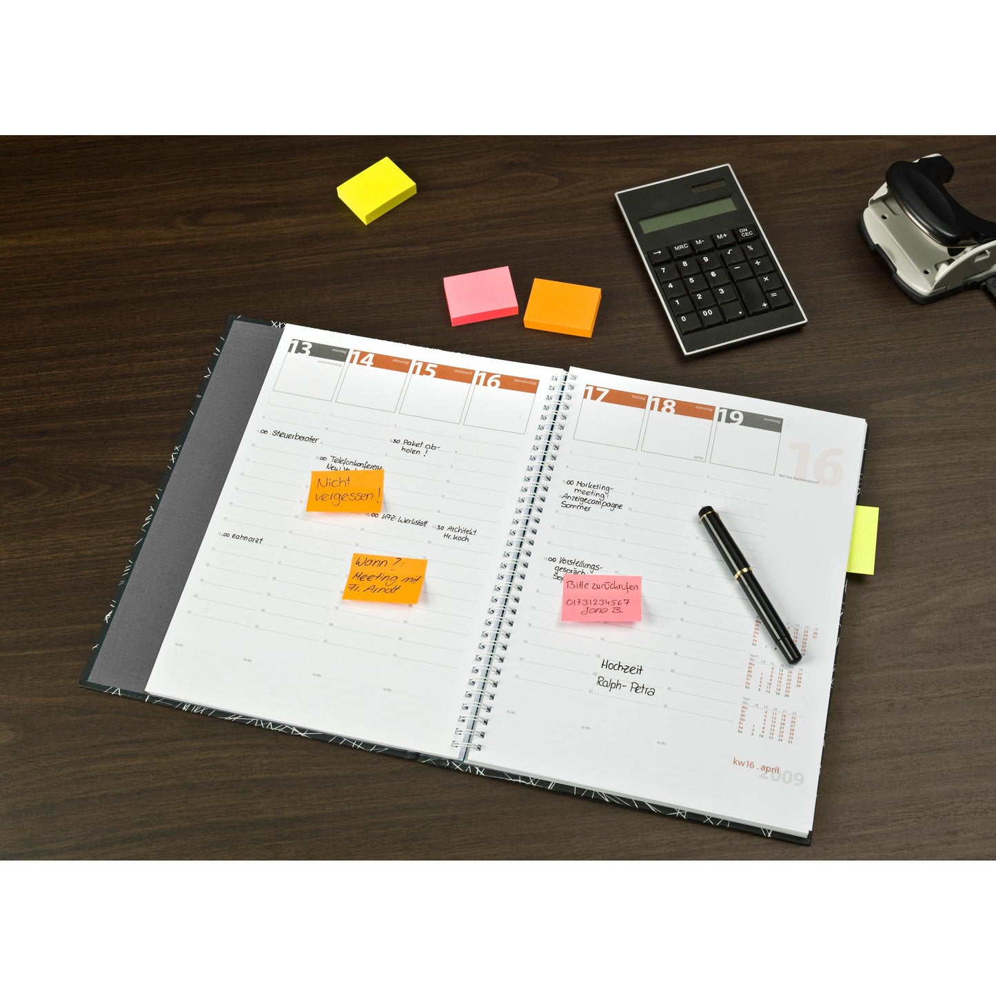 Ein offener Planer mit handschriftlichen Notizen und bunten Post-it® Notes Verschiedene Neonfarben (38 mm x 51 mm, 100 Blatt/Block, 3 Blöcke/Packung, 100% PEFC) von 3M Deutschland GmbH auf einem Holztisch mit Stift, Taschenrechner und Klebebandabroller.
