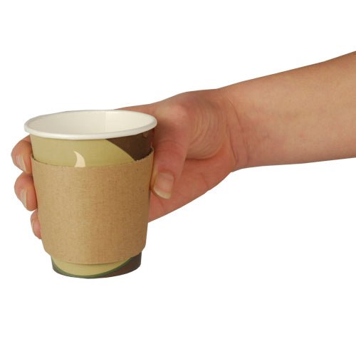 Uma mão segura um copo de papel com bandas PAPSTAR para bebidas quentes "pure", marrom, Ø 7,3 cm com caixa dispensadora (100 unidades) da PAPSTAR GmbH em um fundo branco simples.