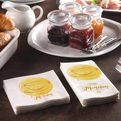 Uma mesa de pequeno-almoço com croissants, uma jarra e 200 PAPSTAR Toalhas de mesa (3 camadas, dobra de 1/4, 24x24 cm) da PAPSTAR Uma GmbH com a inscrição «Bom dia», acompanhada de frascos de compota e três garfos para um pequeno-almoço acolhedor.