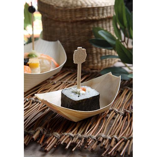 Um pedaço de sushi, envolto em alga marinha e preso com um espeto de madeira, é servido em um barquinho de madeira "pure" da PAPSTAR 50 bandejas para finger food da PAPSTAR GmbH, apresentado sobre uma esteira de palha com folhas e cestos de vime ao fundo.