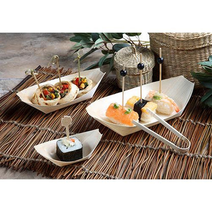 Sushi e aperitivos para finger food são servidos em PAPSTAR 50 bandejas de madeira "pure" "barquinhos" para finger food da PAPSTAR GmbH, cada peça em um espeto decorativo e disposta em jogos americanos de bambu com folhas verdes e cestos trançados ao fundo.