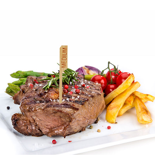 Um bife grelhado com a designação "medium" e o PAPSTAR 250 marcador de bife de 9 cm da PAPSTAR GmbH é servido num prato branco com batatas fritas, espargos, tomates cereja, cebolas vermelhas e ervas – perfeito para a cozinha de restaurante profissional.
