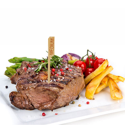 Um bife grelhado com a designação "medium" e o PAPSTAR 250 marcador de bife de 9 cm da PAPSTAR GmbH é servido num prato branco com batatas fritas, espargos, tomates cereja, cebolas vermelhas e ervas – perfeito para a cozinha de restaurante profissional.